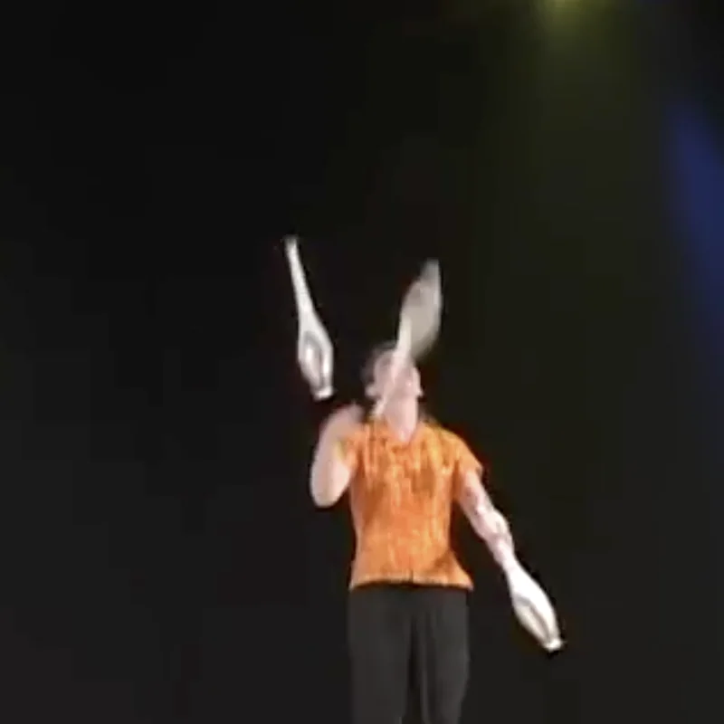 Cindy Marvell juggling three clubs on a dark stage